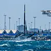 SailGP-katamaran på foil i grov sjø utenfor en industrihavn.