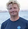 Blond mann i mørk blå t-skjorte med European Yacht of the Year-logo foran havet.