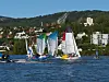 Flere seilbåter i regatta på innsjø med Lillehammer og hoppbakke i bakgrunnen.
