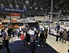 Mennesker beveger seg mellom båter og stands fra Beneteau i en innendørs messehall.