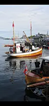 En restaurert fiskeskøyte ligger i havna med norske flagg og bygninger langs kaia i bakgrunnen.