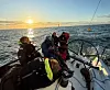 Mannskap i seilbåt på åpent hav i solnedgang