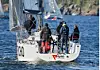 Seilbåt med mannskap på dekk seiler nær steinete kyst