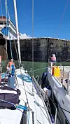 Seilbåter i smal sluse med mannskap som holder tau mot høy betongvegg
