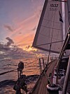 Seilbåt på åpent hav under dramatisk solnedgang med heiste seil.