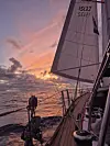 Seilbåt på åpent hav under dramatisk solnedgang med heiste seil.