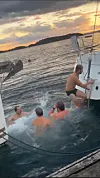 Fire personer bader i sjøen ved en båt ved solnedgang.