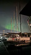 Fortøyd seilbåt ved brygge med grønt nordlys på nattehimmelen.