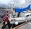 Seilbåt ved kai med norsk flagg, blå presenning og en person på dekk i småbåthavn.
