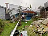 Ødelagt hagestue med bøyd tak og veltede gjenstander i en våt hage etter uvær.