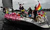 Pyntet seilbåt med regnbueflagg, ballonger og rosa dekor på vannet.