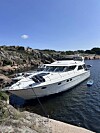 Hvit motorbåt fortøyd ved svaberg i solskinn.