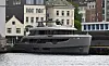 Stor grå yacht fortøyd ved kaien foran bygninger langs en byhavn.