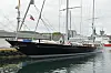 Stor seilyacht med svarte skrog og høye master ligger fortøyd ved kai i en havn.