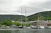 Stor seilbåt med flere master ligger ved kai foran en by med grønne åser i bakgrunnen.