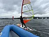 Windsurfer på mørkt vann med blå oppblåsbar brygge i forgrunnen og flere seil i bakgrunnen.