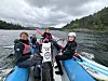 Fire personer sitter på en seilbåt med rød seilbom på vannet under en overskyet himmel.