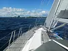 Utsikt fra seilbåtdekk mot hav og kystlinje under blå himmel med skyer.