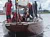 Seilbåt med flere personer om bord ved en brygge, med seil, mast og tauverk.