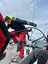 Personer om bord på en seilbåt jobber med tauverk under vindfulle forhold.