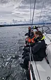 Personer sitter på en seilbåt på åpent vann under en grå himmel.
