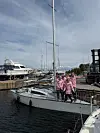 Gruppe i rosa klær står på en seilbåt ved en brygge i en marina.