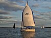 Seilbåt med hvit spinnaker på rolig vann ved solnedgang.