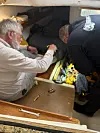 To personer utfører vedlikehold i et trangt rom om bord med verktøy på gulvet.