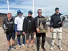 Fem menn står på en brygge og viser fram en innrammet premie ved sjøen.