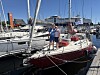 To personer står på en rød seilbåt i en marina omgitt av andre båter.