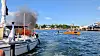 Flammer og svart røyk kommer fra en båt i en havn med andre båter i nærheten.