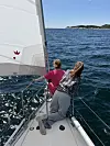 To personer på fordekket av en seilbåt trekker i tau mens et hvitt seil fylles av vind.