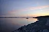 En seilbåt på stille vann ved en steinete kyst i kveldssol.