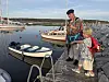 To personer står på en steinmolo ved småbåter fortøyd i en rolig havn.