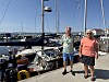 To menn står på en brygge foran seilbåter i en småbåthavn.