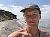 Bror Sonne står solbrun på en strand på tunø i danmark. Han har på caps. bak er en klippe. landskapet er fremmed, langt hjemmefra