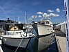 Hvite båter ligger fortøyd i en marina med blå himmel og brygger.