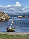Liten fargerik båt på en strand ved steinete kyst og blå sjø.
