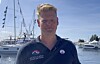 Mann i mørk poloskjorte foran seilbåter i en marina.