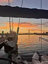 Fortøyde seilbåter ved en marina foran en oransje solnedgang over stille vann.
