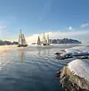 Flere seilbåter på stille vann med snødekte svaberg og kystlandskap i bakgrunnen.